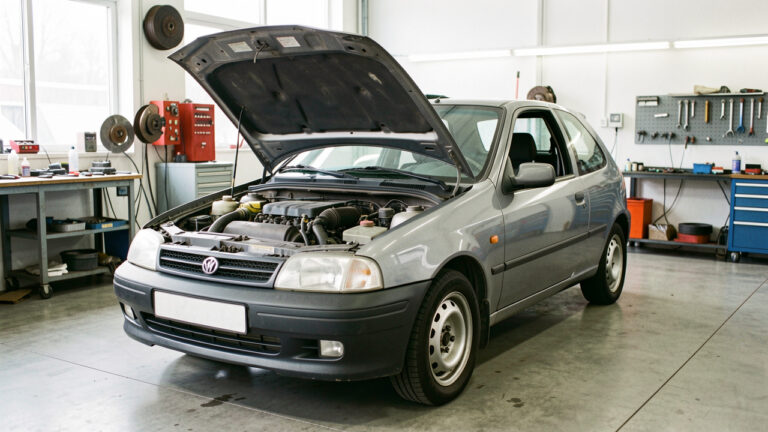 Voiture compacte d’occasion inspectée dans un atelier, avec le capot ouvert et les principaux éléments mécaniques visibles.